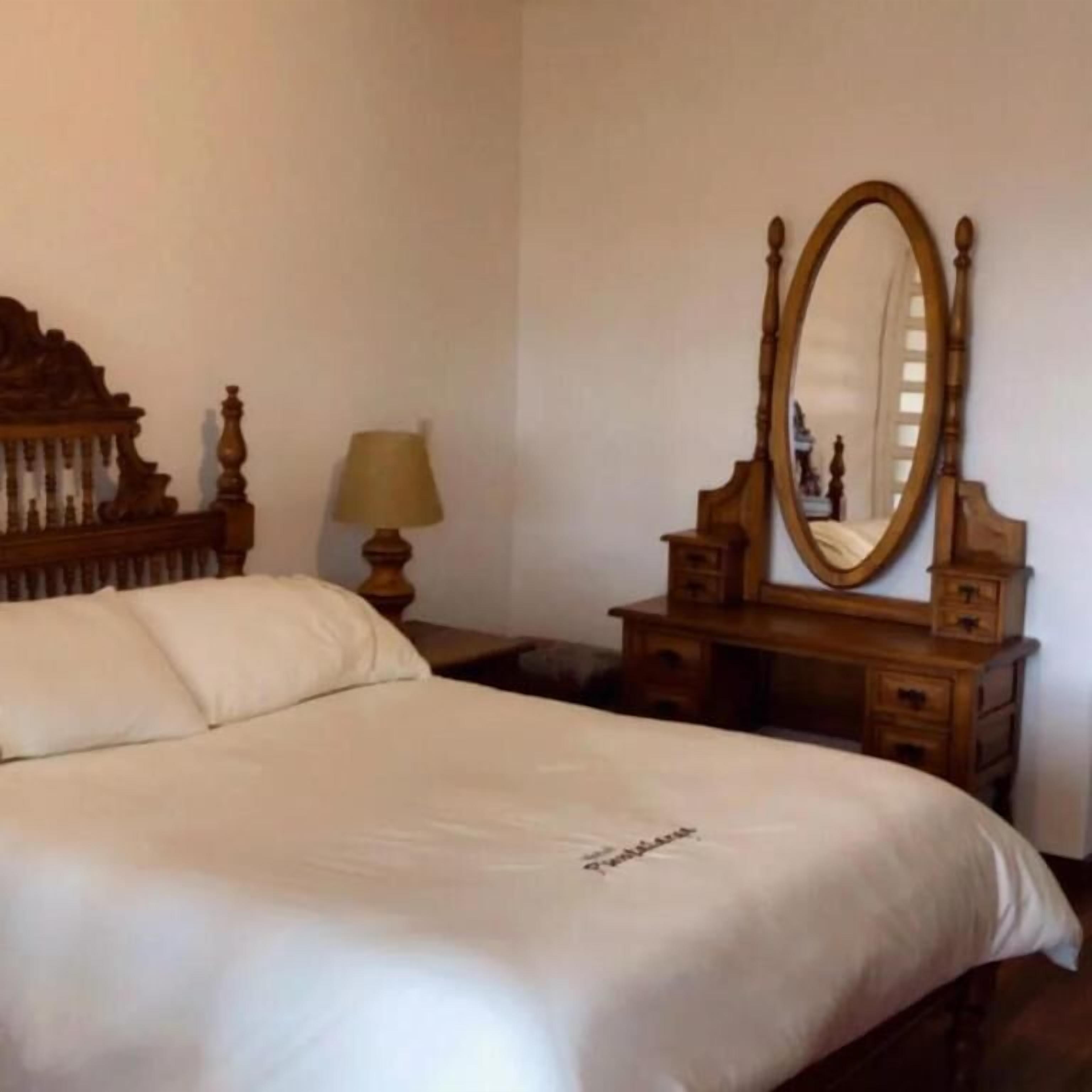 A neatly made bed with a wooden headboard, a bedside table with a lamp, and a mirror.