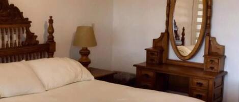 A neatly made bed with a wooden headboard, a bedside table with a lamp, and a mirror.