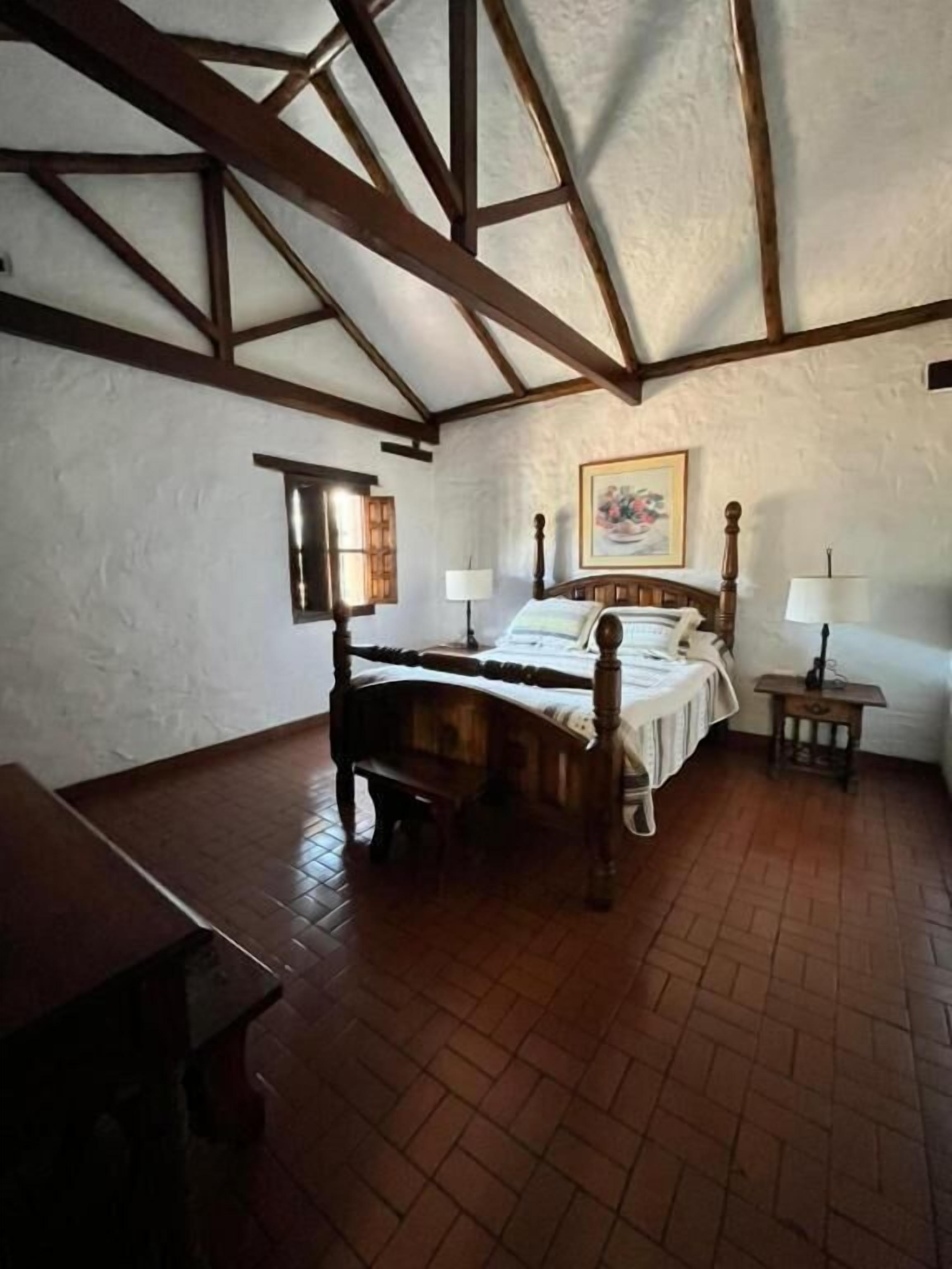 A bedroom with a wooden bed, a small bedside table, a nightstand, and a window with curtains.