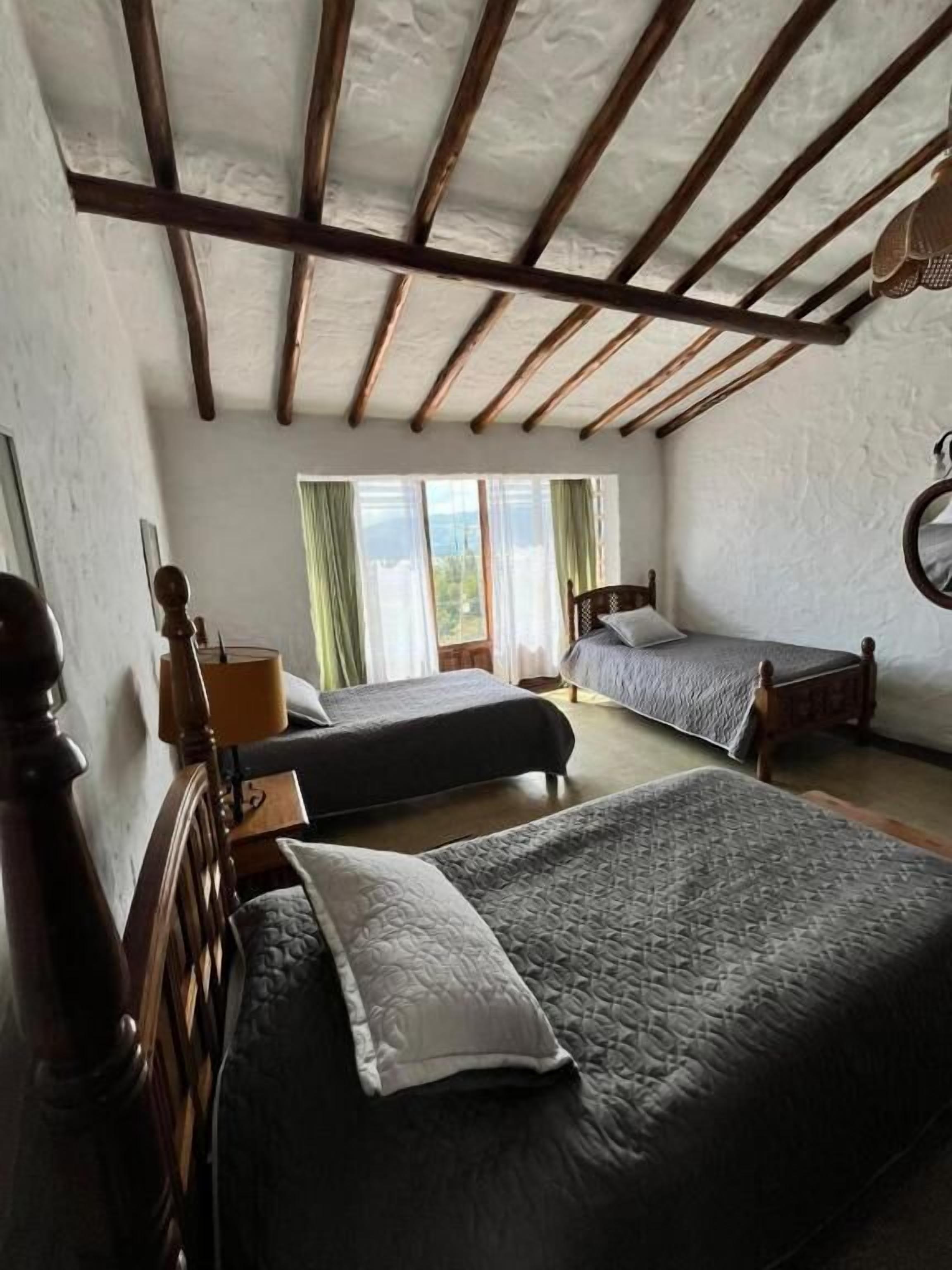 Een slaapkamer met twee bedden, een houten hoofdbord, een raam met gordijnen en een houten plafond.