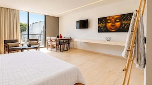 Ein modernes Hotelzimmer mit einem großen Bett, einem Esstisch, Stühlen, einem Fernseher und einem großen Fenster.