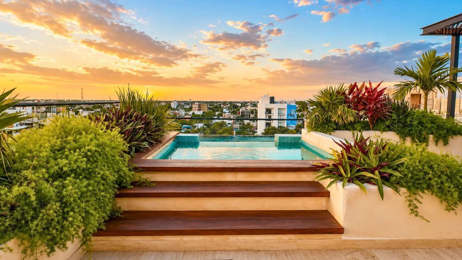 Une piscine sur le toit, accessible par des marches, entourée d’une végétation luxuriante et offrant une vue sur le paysage urbain au coucher du soleil.