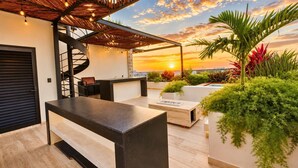 Una terraza en la azotea con una escalera en espiral, mobiliario exterior y vistas al atardecer.