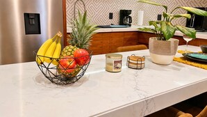 Una encimera de cocina con una cesta de fruta, una vela y una cafetera.