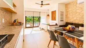 A modern kitchen with a granite countertop, a dining area with a table and chairs, a ceiling fan, and a stone wall. - Bright Balcony Studio Beach Vibe · Blanko Living (Playa del Carmen)