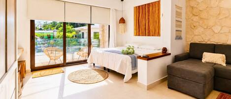 Une chambre moderne avec un lit, un coin salon et une vue sur l’extérieur, accessible par une porte coulissante.