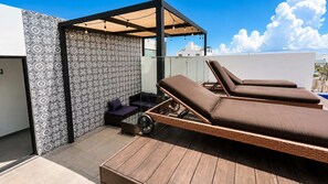 Eine Dachterrasse mit zwei Liegestühlen und einer kleinen Sitzecke, mit gemusterten Wänden und einem Holzboden.