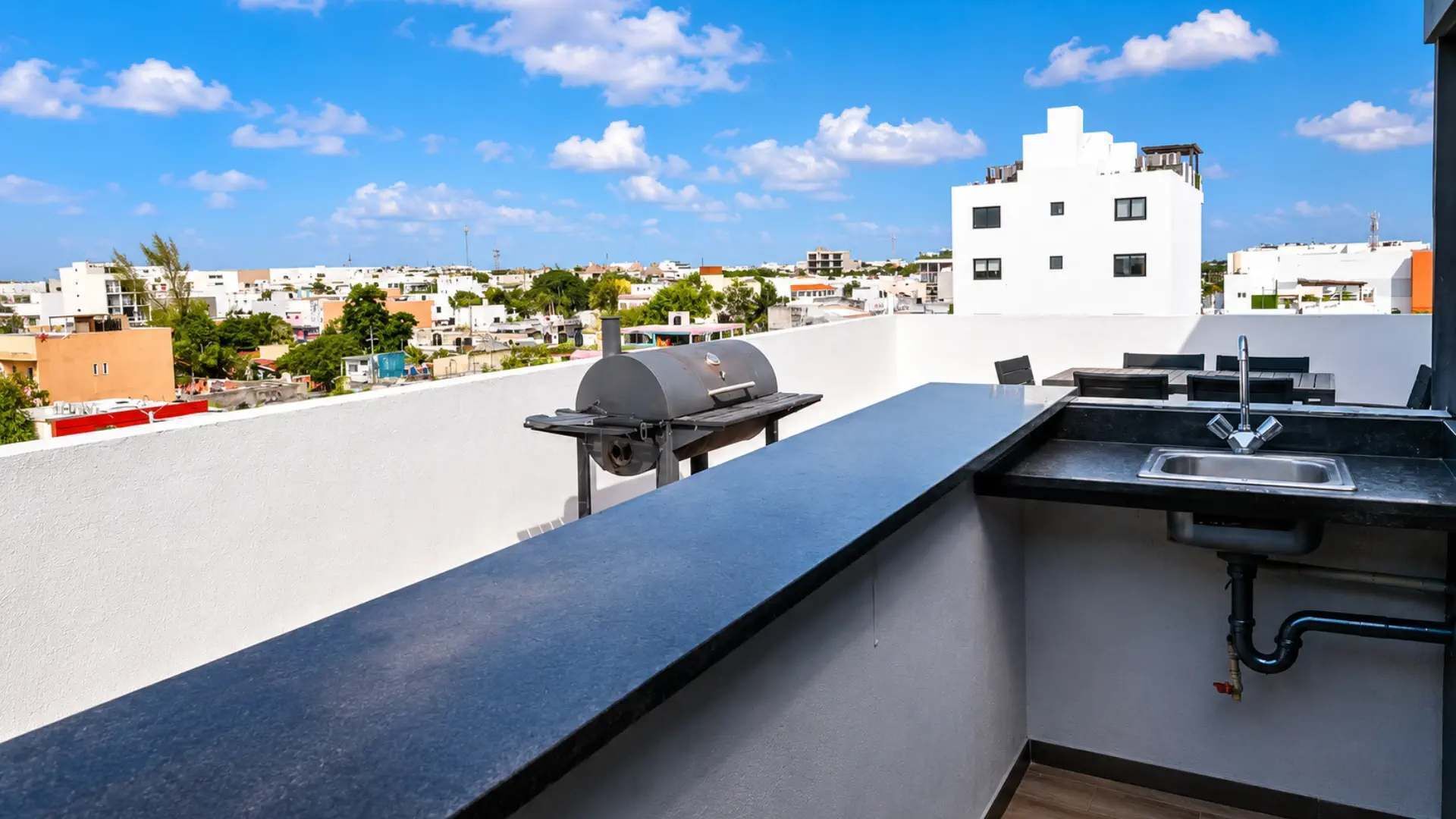 A rooftop terrace with a grill, sink, and a view of the cityscape.