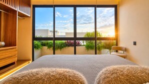 Ein Schlafzimmer mit großem Fenster, einem Bett mit weichen Kissen, einem Holzschrank und einem Sessel.