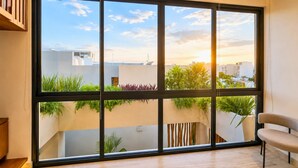 Ein Zimmer mit großem Fenster, einem Sessel und Blick auf Gebäude und Grünflächen.