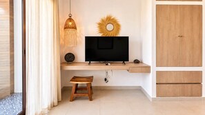 Ein modernes Zimmer mit einem Fernseher auf einem Holzständer, einem kleinen Hocker, einem dekorativen Sonnenstrahlspiegel und einer hängenden Leuchte.