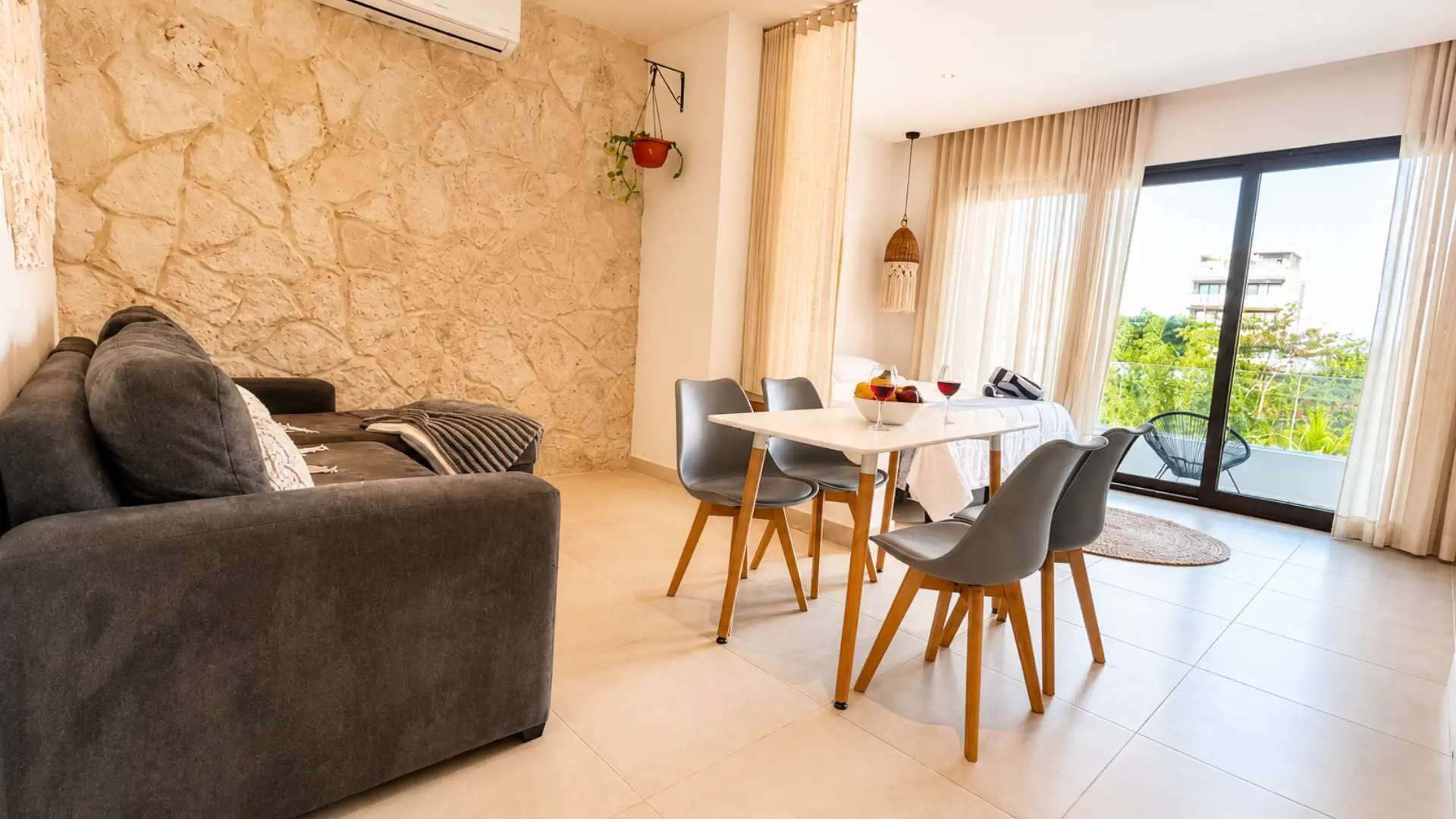Uma sala de estar moderna com uma parede de pedra, um sofá, uma mesa de jantar com cadeiras e vista para o verde através de grandes janelas.