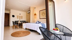 Ein modernes Schlafzimmer mit Bett, einer Essecke mit Tisch und Stühlen sowie einem Balkon mit Stuhl und Obstschale.