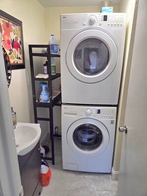A compact laundry room with two stacked washing machines, a sink, and a shelf with cleaning supplies. - 2-bedroom house in pleasant Tampa with cool AC and comfort (Tampa)