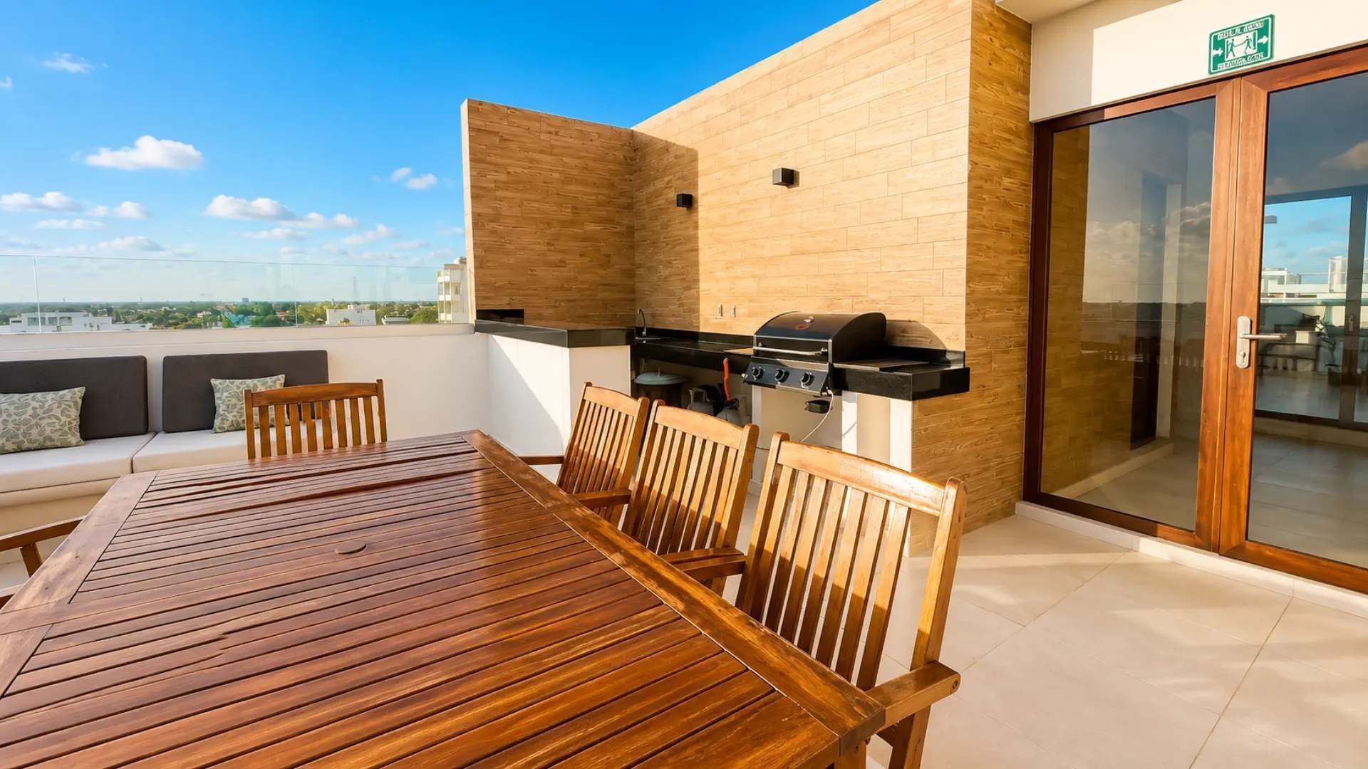 Une terrasse sur le toit avec une table et des chaises en bois, un barbecue et une porte vitrée.