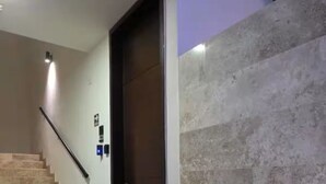 Un escalier menant à une porte surmontée d’un paillasson, avec une rampe et un mur à surface texturée.
