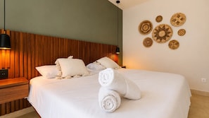 A neatly made bed with white linens and rolled towels, a wooden headboard, and decorative wall art. - Cute Sea View  Balcony Apartment · Musa del Carmen (Playa del Carmen)
