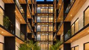 A multi-level atrium with wooden beams and glass railings, featuring indoor plants and natural lighting. - Cute Sea View  Balcony Apartment · Musa del Carmen (Playa del Carmen)