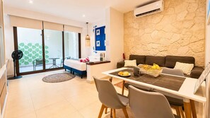 Ein modernes Wohnzimmer mit einer Couch, einem Esstisch und Stühlen. Es gibt einen Balkon mit Aussicht, einen Ventilator und eine Wand-Klimaanlage.