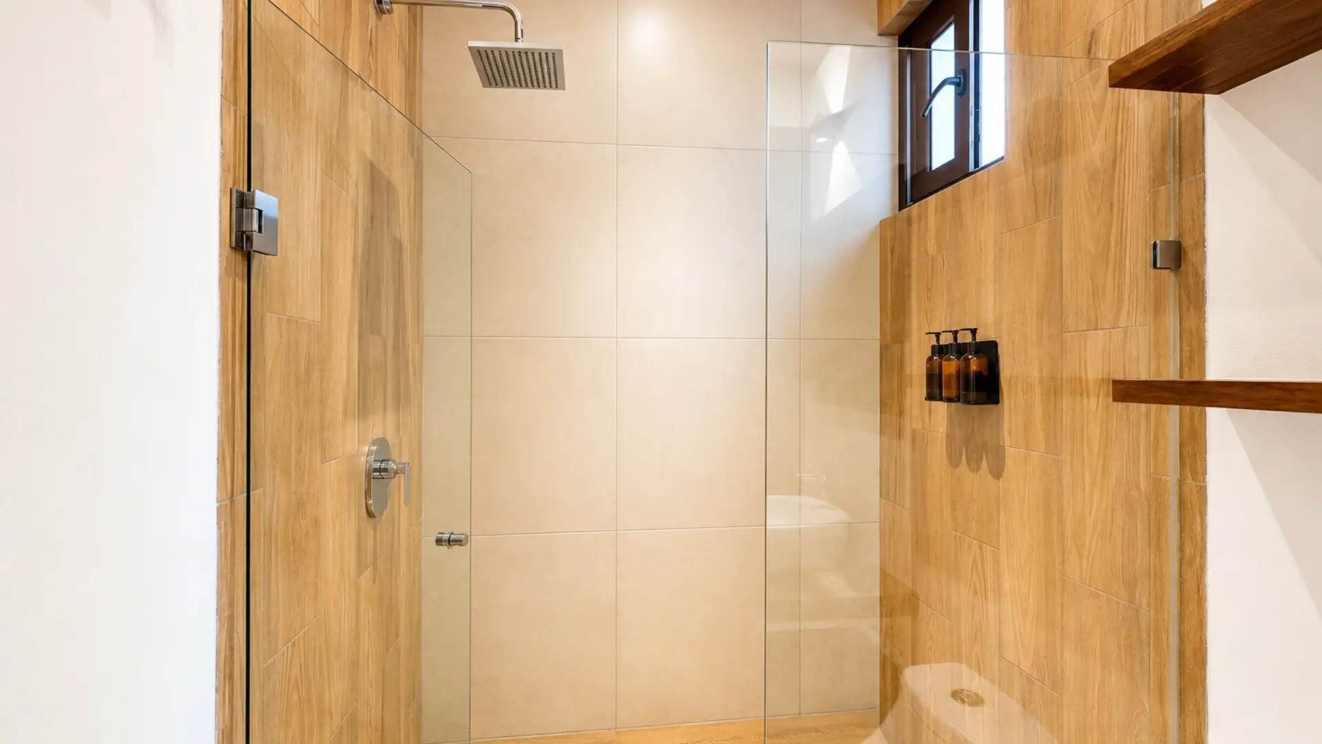 Una doccia moderna con porta in vetro, pannelli di legno e una piccola finestra.