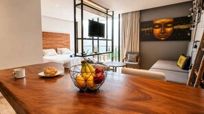 Ein Hotelzimmer mit einem Holztisch, einer Obstschale, einem Bett, einem Fernseher und einem Bild an der Wand.