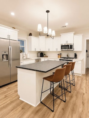 A modern kitchen with white cabinetry, a stainless steel refrigerator, a built-in microwave, and a central island with bar stools.