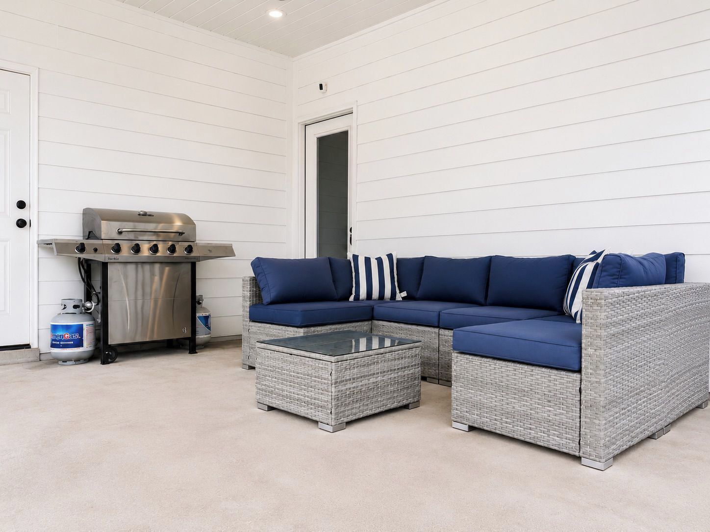 Un espace extérieur aménagé, abrité et doté d’un canapé d’angle, d’une table basse en verre et d’un barbecue.