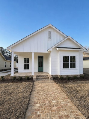 A single-story house with a front porch, a green door, and a brick pathway leading to the entrance.