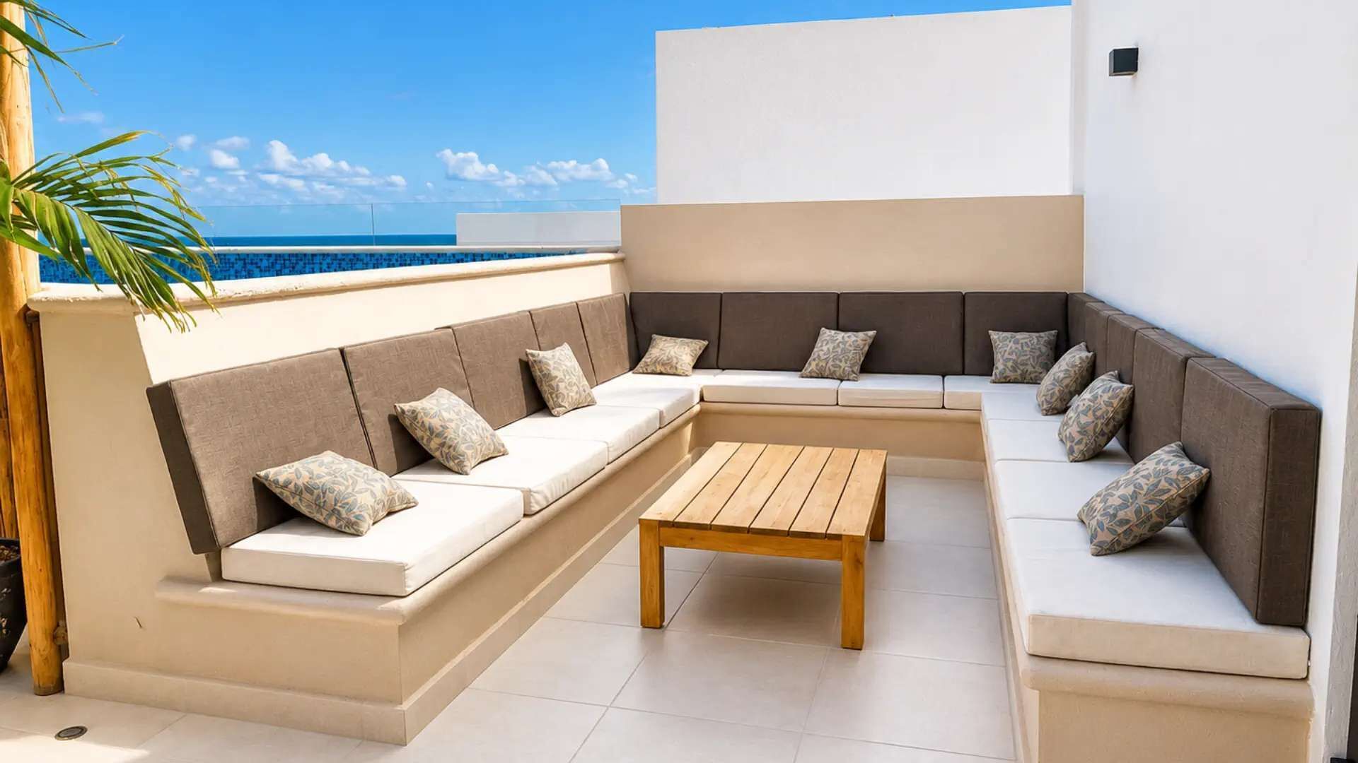 Un rincón con asientos, una mesa de madera, cojines color beige y vista al océano.
