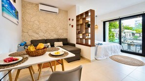 A modern living room with a stone wall, a sofa, a dining table with a fruit bowl, and a view through a large window. - Relaxed Studio with  Hammock · Blanko Living (Playa del Carmen)
