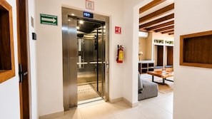 An elevator with a sign indicating the evacuation route, a fire extinguisher, and a wooden ceiling structure. - Relaxed Studio with  Hammock · Blanko Living (Playa del Carmen)