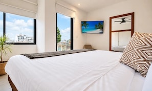 Ein Schlafzimmer mit einem großen Bett, Blick auf die Stadt durch ein Fenster, einem Deckenventilator und einem Strandbild.