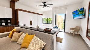 A modern living room with a sofa, a coffee table, a TV, and a kitchen area with cabinets and a countertop. - Dreamy Rooftop Pool Studio near Beach · Cosmo 42 (Playa del Carmen)