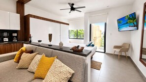Ein modernes Wohnzimmer mit Sofa, Couchtisch, Fernseher und Küchenzeile mit Schränken und Arbeitsplatte.