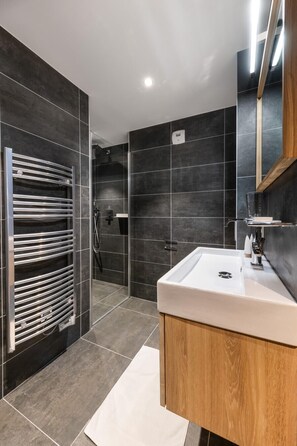 A modern bathroom with a large mirror, a white sink, and a towel rack. - Steamboat by Alpine Resorts (Courchevel)