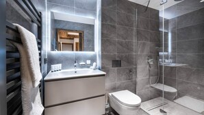 Een moderne badkamer met een douchecabine van glas, een wastafel met spiegel en een toilet.
