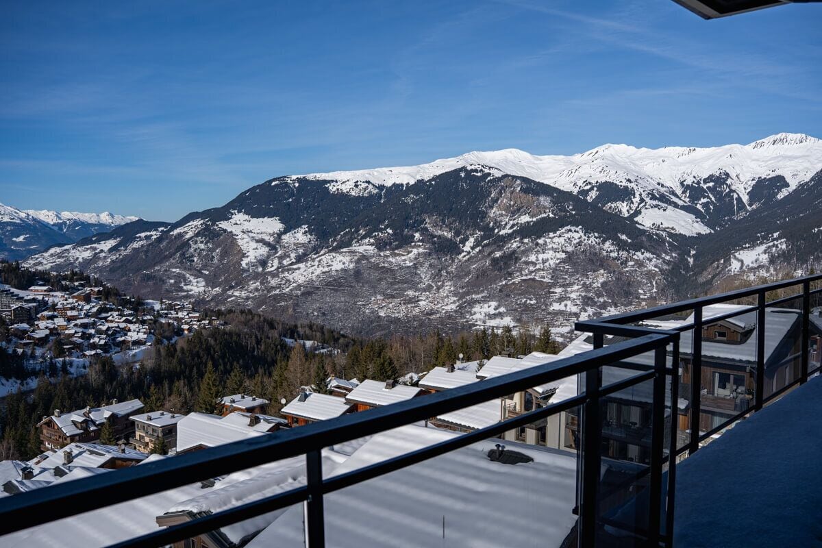 Paisaje montañoso con picos nevados y una zona residencial en la parte baja.