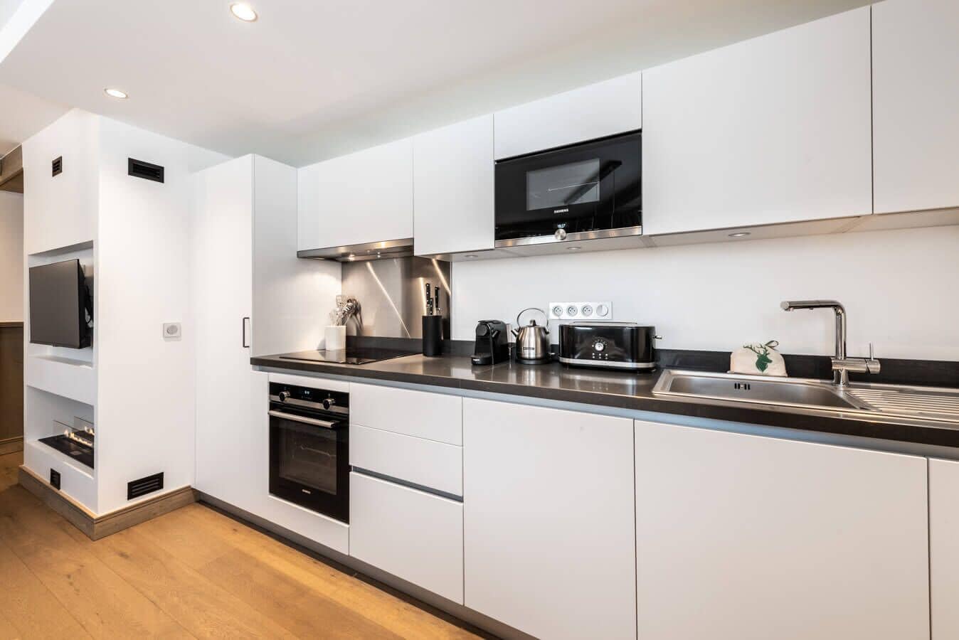 A modern kitchen with built-in appliances, a flat-screen TV, and a stainless steel sink.