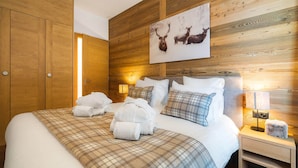 Een hotelkamer met een houten hoofdeinde, een bed met geruit beddengoed, twee nachtlampen en een schilderij van een herten aan de muur.