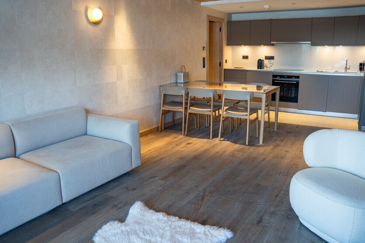 Una sala de estar moderna con un sofá, una mesa de comedor con sillas y una cocina al fondo.