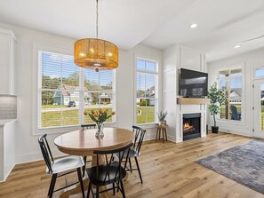 Ein großzügiges Wohnzimmer mit Kamin, einem runden Esstisch und großen Fenstern mit Blick ins Freie.