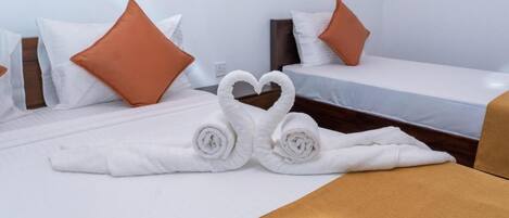 A hotel room with two beds, white bedding, brown pillows, and a heart-shaped towel arrangement.