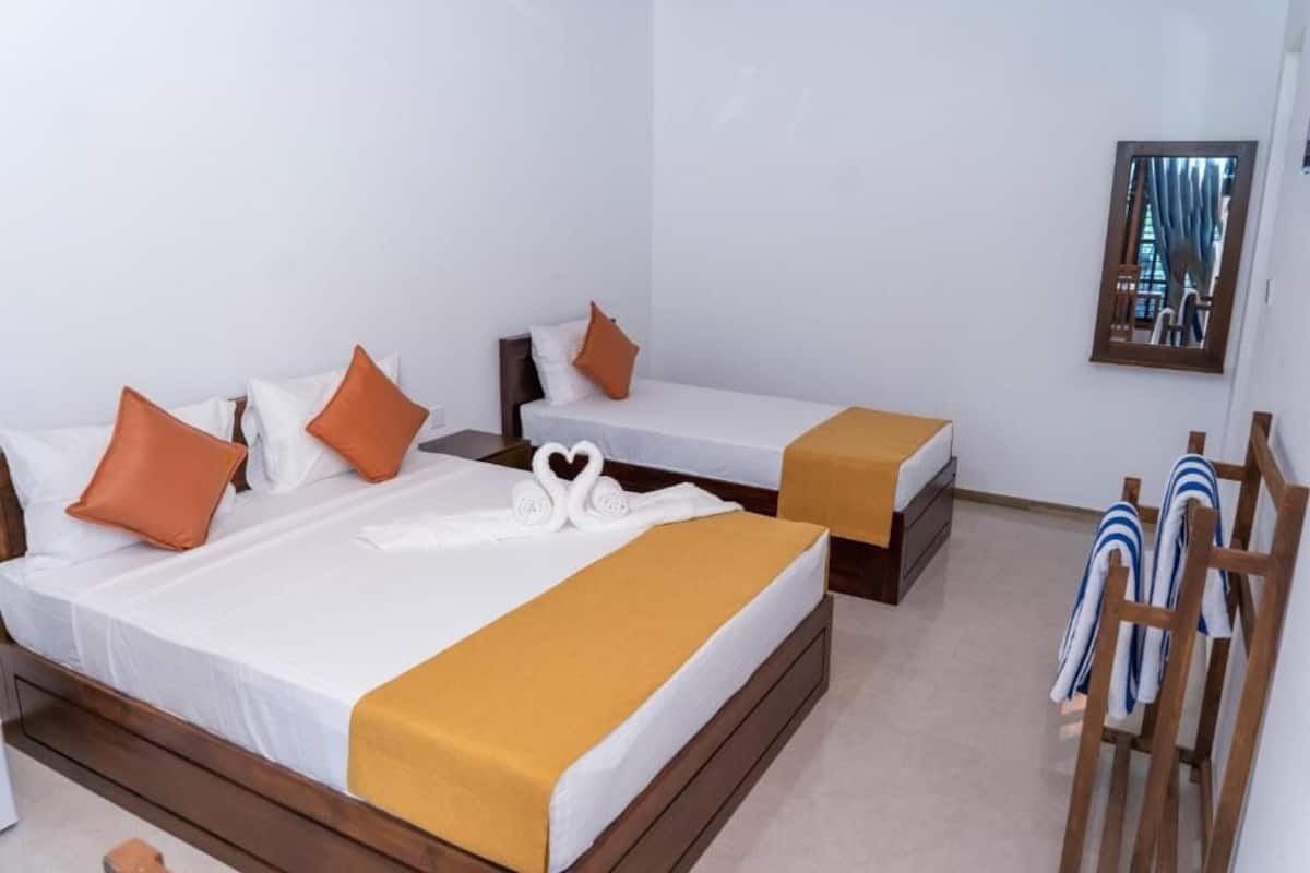 A hotel room with two beds, a wooden headboard, a towel rack, and a window with curtains.
