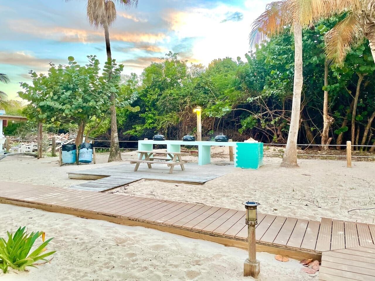Un espace aménagé au bord de la plage, avec une terrasse en bois, des tables de pique-nique et des barbecues.