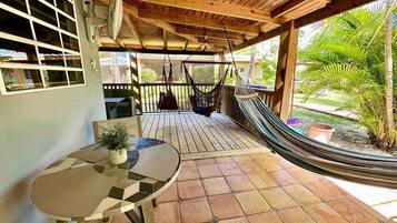Een overdekt terras met een ronde tafel, een hangmat en uitzicht op groen.