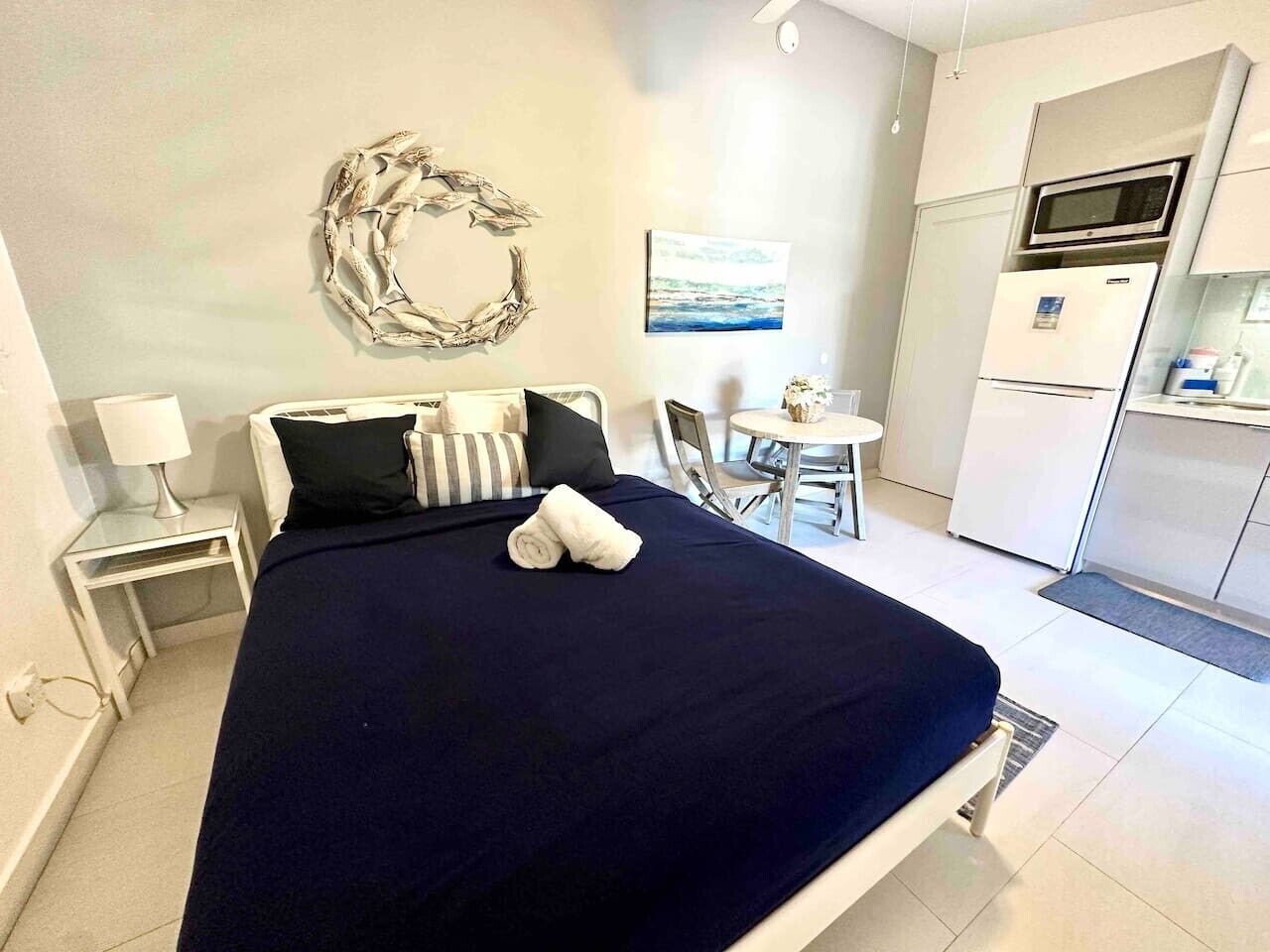 A hotel room with a bed, a small table, a chair, a microwave, and a refrigerator.