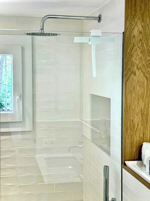 A glass-enclosed shower with a rain showerhead, a window with a view of trees, and a wooden panel on the right side. - Designed Costa Brava apartment with sea views (Girona)