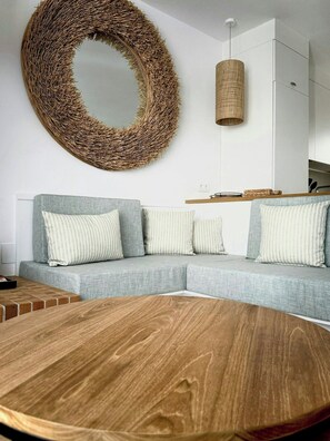 A modern living room with a sectional sofa, a round woven mirror, a hanging woven light fixture, and a wooden coffee table. - Designed Costa Brava apartment with sea views (Girona)