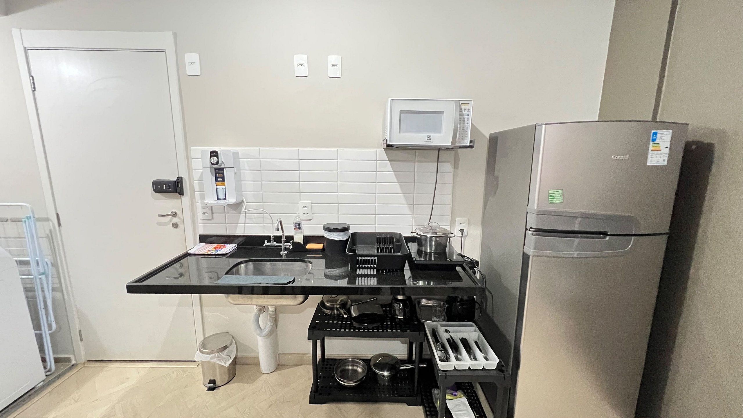 Uma cozinha compacta equipada com geladeira, micro-ondas, pia e cafeteira.