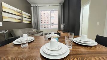 A dining area with a wooden table set for four, a sofa, and a view of buildings through a window.